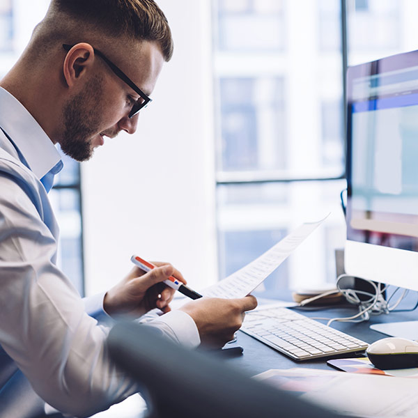 Man reading a paper  document at a computer